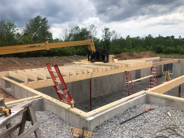 Early‑stage new home construction with concrete foundation walls and floor framing in progress by Fournier Construction &amp; Excavation.