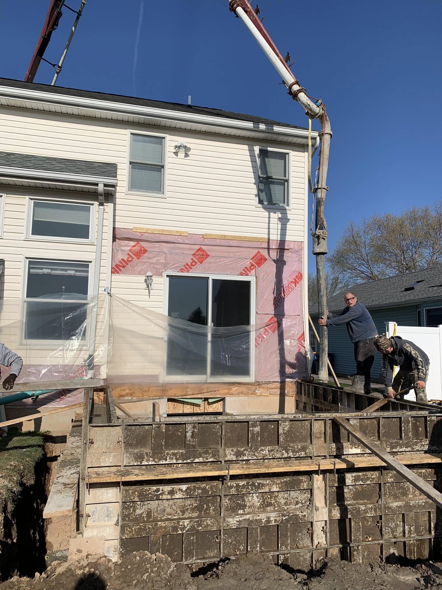 Concrete being pumped into a new foundation area for a home addition, with workers guiding the hose and formwork in place.