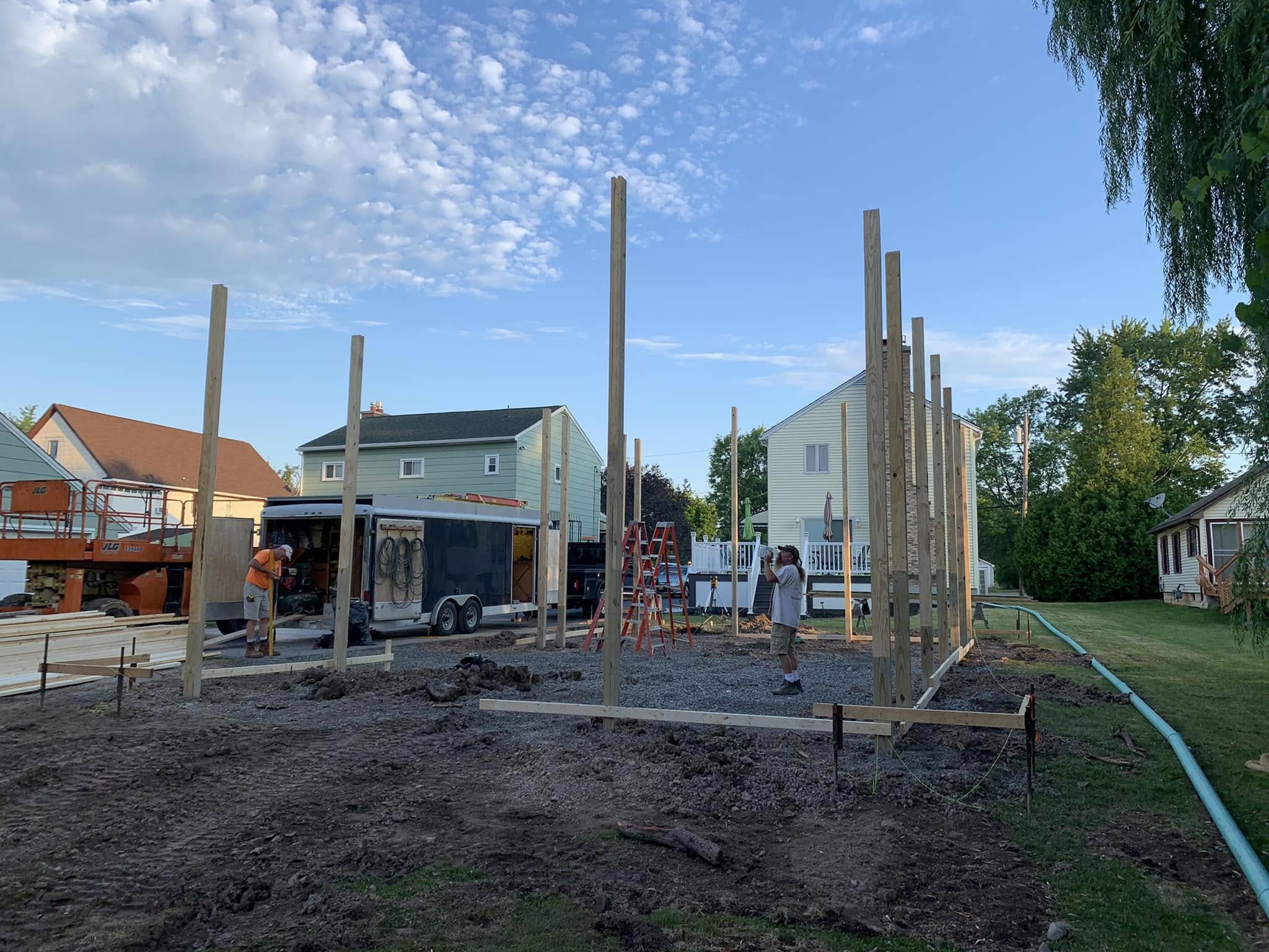 Early stage of post‑frame construction with vertical posts set in gravel base and crew working on site.
