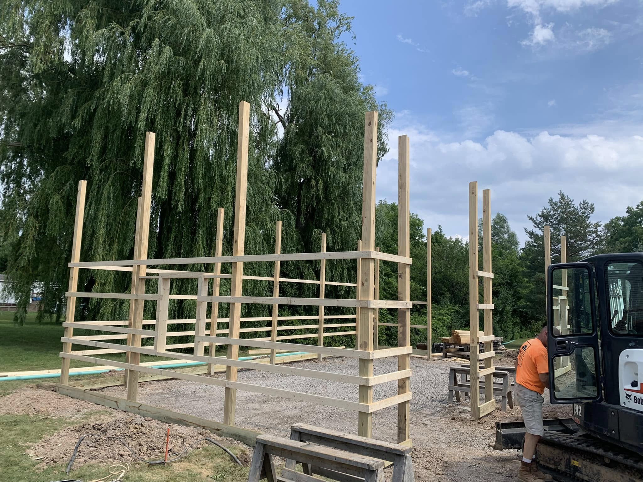 Wooden framework for post‑frame building going up with vertical posts and horizontal beams in place.
