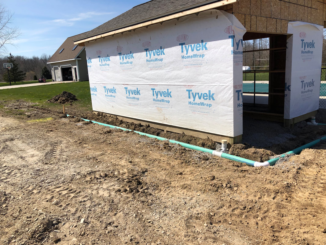 Tyvek‑wrapped structure with drainage pipes installed around foundation during excavation work.