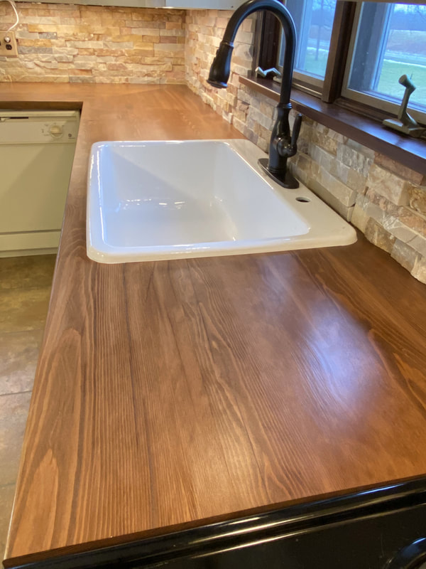 Reclaimed barn‑wood countertop with farmhouse sink and stacked‑stone backsplash in rustic kitchen remodel.