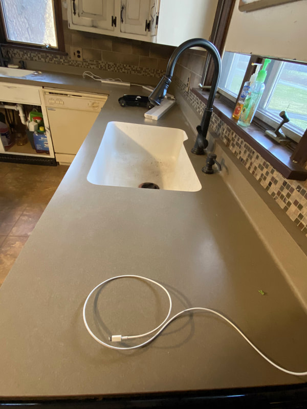 Kitchen sink area during remodel with solid‑surface temporary countertop and backsplash prep work before installing reclaimed barn‑wood counters.