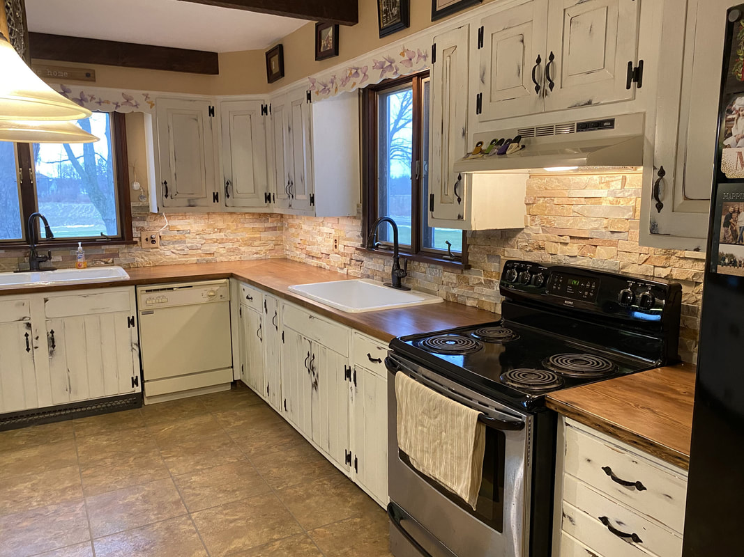 Rustic kitchen with distressed white cabinets, stacked‑stone backsplash, and reclaimed barn‑wood countertops